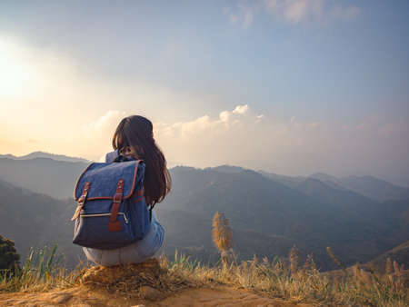 backside of woman with backpack sitting to enjoy on mountains peak in the morningの写真素材