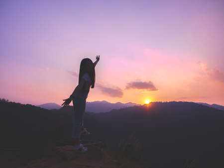 Silhouette of woman enjoying the sunset with dramatic sky on mountain peak.の写真素材