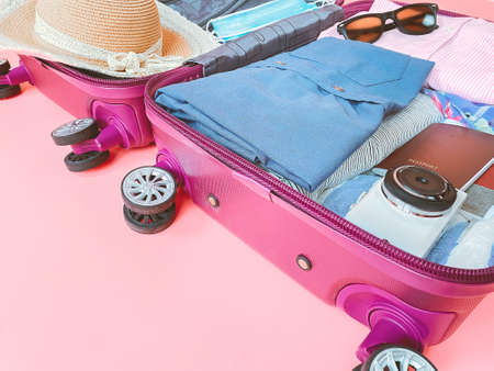 suitcase bag with clothing and mask on pink background. summer vacation travel with virus pandemic.の写真素材