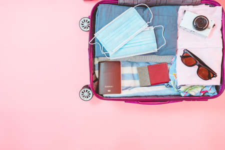 suitcase bag with clothing and mask on pink background. summer vacation travel with coronavirus pandemic.の写真素材