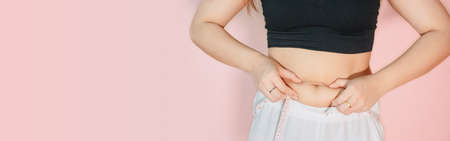 Lose belly fat concept from close up woman in sportswear with hand holding her own belly fat and...