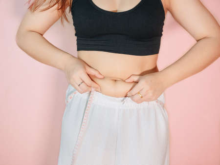 Lose belly fat concept from close up woman in sportswear with hand holding her own belly fat and cellulite.の写真素材