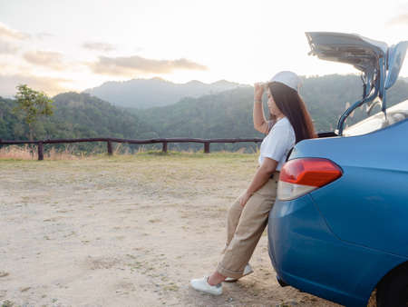 Young asian woman traveler parked car on viewpoint with enjoying the beautiful landscape during sunset.  road trip conceptの写真素材