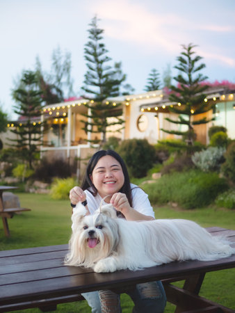 Cheerful Asian woman and Shih Tzu dog in front of hotel with lush garden in the evening