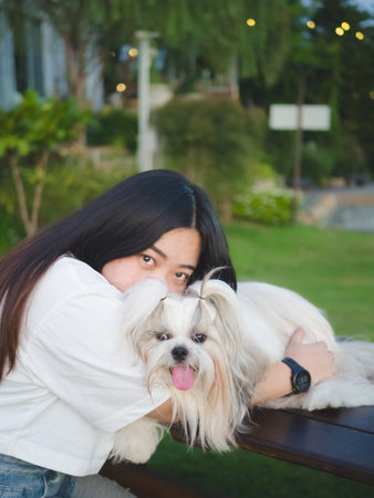 Cheerful Asian woman and Shih Tzu dog in front of hotel with lush garden in the eveningの写真素材