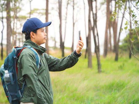 Solo adventure Asian traveler man with backpack on hiking trip in forest and using smartphone.