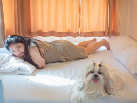 Asian woman relaxing on bed with her Shih Tzu dog in cozy bedroom. Simple happiness and home lifestyle concept.の写真素材