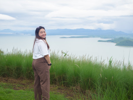 Confident curvy Asian woman smiling in nature with lake and mountain background.の写真素材