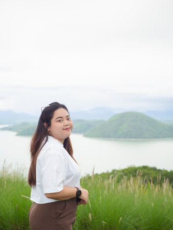 Confident curvy Asian woman smiling in nature with lake and mountain background.の写真素材