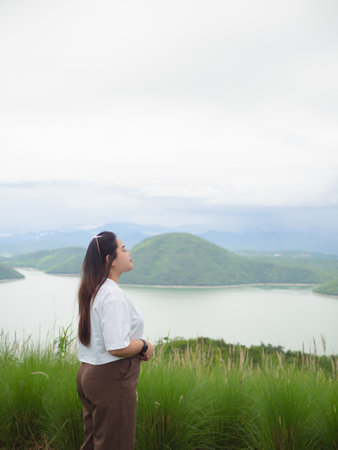 Confident curvy Asian woman smiling in nature with lake and mountain background.の写真素材