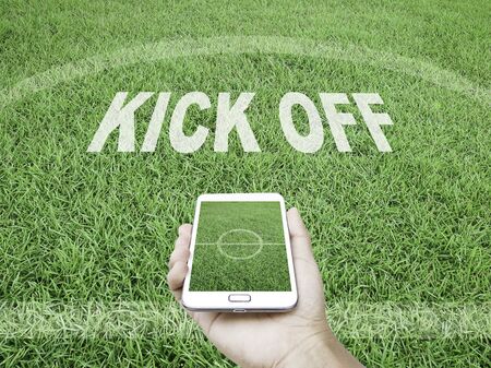 Phone and football concept,Hand holding mobile smart phone with a football field as background.の写真素材