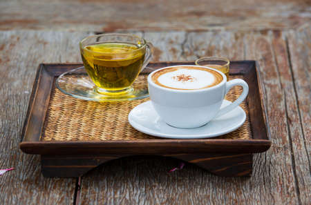 Coffee and tea cups are placed on a rattan tray on a wooden table in a coffee shopの写真素材