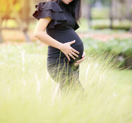 Portrait of a happy pregnant woman touching her belly with hands in a parkの写真素材