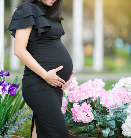 Portrait of a happy pregnant woman touching her belly with hands in a park