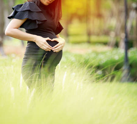 Portrait of a happy pregnant woman touching her belly with hands in a parkの写真素材