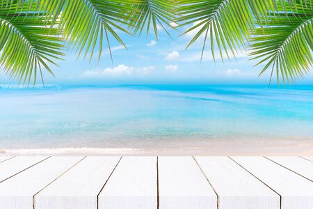 Top of wood table with seascape and palm leaves, blur bokeh light of calm sea and sky at tropical beach background.blurred blue sky and sea with bokeh light and old wooden table backgroundの写真素材