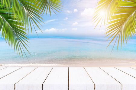 Top of wood table with seascape and palm leaves, blur bokeh light of calm sea and sky at tropical beach background.blurred blue sky and sea with bokeh light and old wooden table backgroundの写真素材