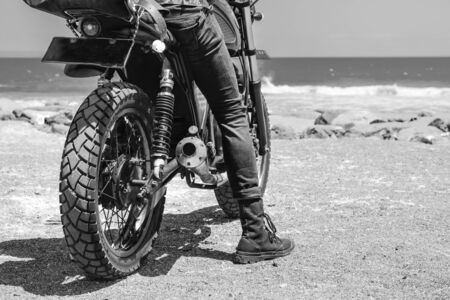 A person sitting on the motorcycle while looking at the oceanの写真素材