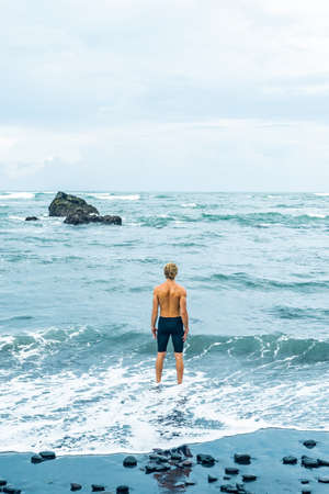 Figure of a shirtless man standing with back in ocean wavesの写真素材