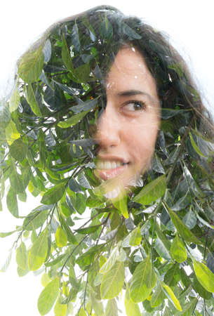 A double exposure of a half smiling young womans portrait and green tree leaves