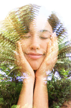 A double exposure portrait of a half smiling young woman with eyes closed holding her chin with...