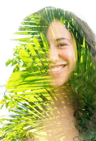 A double exposure of a smiling young womans portrait and palm tree leaves