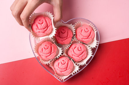 Hand holding a heart-shaped cookie box of pink meringue cakes