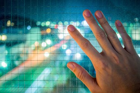 a hand is on the window which is protected by wire net at nightの写真素材
