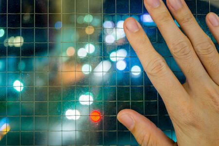 a hand is on the window which is protected by wire net at nightの写真素材