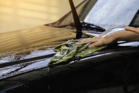 hand women hold water over the black car for washing with microfiber clothの写真素材