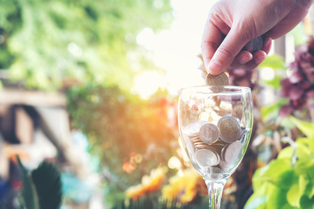 Hand women putting money (coins) in the glass. Investment and Interest Concept. Filter soft effect and warm sunset selective focus.の写真素材