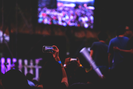 Hand with a smartphone records live music festival, Taking photo of concert stage, live concert, music festival, happy youth, luxury party, landscape exterior - purple light, mountain thailandの写真素材