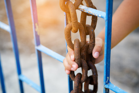 Hands a young child clutching prison bars - Selective focus. Hand holding on chain cage on bulr background.の写真素材