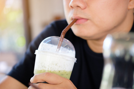 A young man is using a straw to drink from a green milk tea cup on handの写真素材