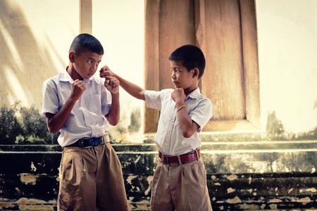 Two asian boys wearing school uniforms are playing boxing, old wall temple background Local Thailandの写真素材