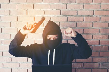Hacker holding gun working on his computer, war, terrorism , terrorist and bandit concept. Glitch...