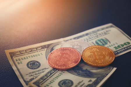 Three symbolic coins of bitcoin on banknotes of one hundred dollars. Exchange bitcoin cash for a dollar. Profit from trading on the stock exchange cryptocurrencies. Earnings on the growth of bitcoin.の写真素材