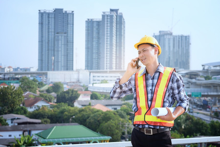 Man Engineers stand on tall buildings and talk about cell phones in the field of construction. Engineers are meeting, working and looking at drawing in mobile, building backgroundの写真素材
