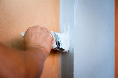 Selected focus hand of worker holding brush painting white color to the concrete orange wall, New home construct or build houseの写真素材