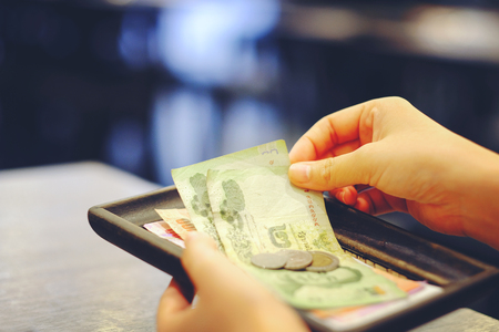 Close-up hand holding of Bill with Thai money banknote and coins (Tip) on cash receipt change from the restaurantの写真素材