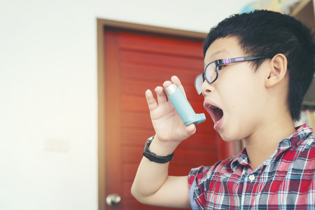 child with spray, boy using his asthma pump inhaler at home, allergy conceptの写真素材
