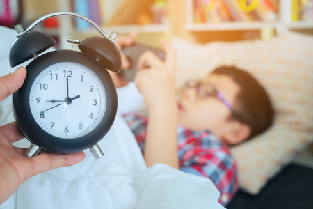 Hand show out for alarm clock on morning, boy playing in the game on the phone lying lazy in bedの写真素材