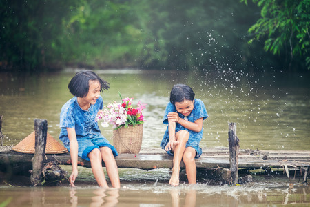 Two gril children sitting and playing water together on wooden bridge over swamp, Asian kids playing waterの写真素材