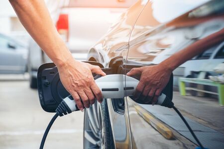 Hand hold of charging modern electric car battery on the street which are the future of the Automobile, Close up of power supply plugged into an electric car being charged for hybrid . New era of vehicle fuel.の写真素材