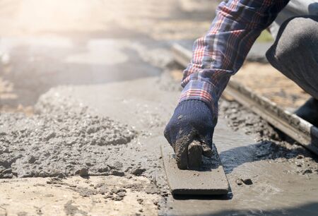 Close up of construction worker's gloved hands using trowel to scrape excess mix level with wood...
