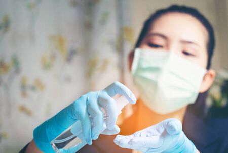 Coronavirus. Woman cleaning her hands at the office. Sick with mask for corona virus. Woman spraying...