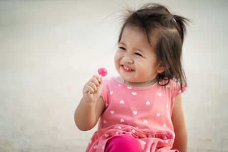 Little child girl enjoy eating lollipop candy, kid Thailandの写真素材