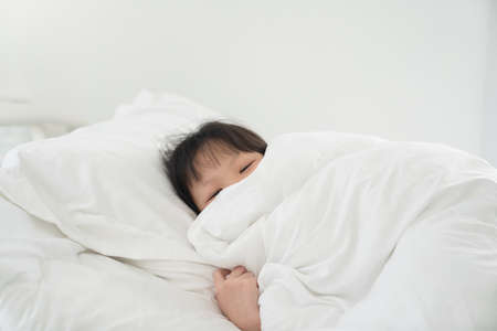 Cute asian girl lying under blanket on white bed