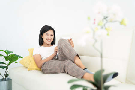 Young lady with modern laptop sitting on sofa at home