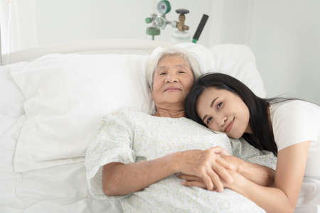 close up of patient grandfather and women holding hands in hospital bedの写真素材